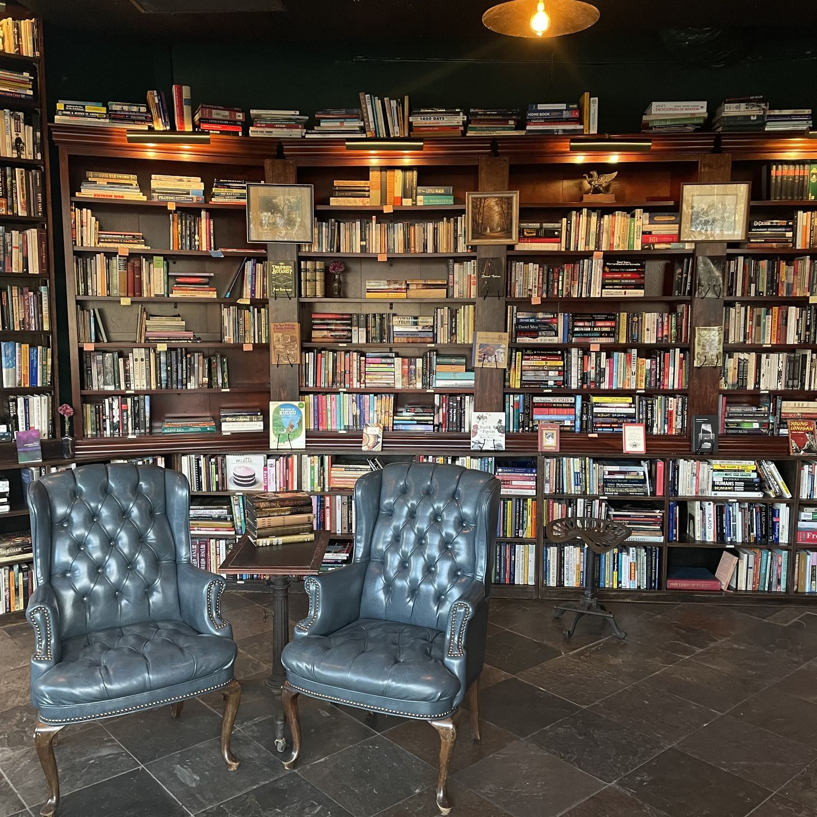 Two blue tufted leather wingback chairs in front of a wall of dark wood bookshelves