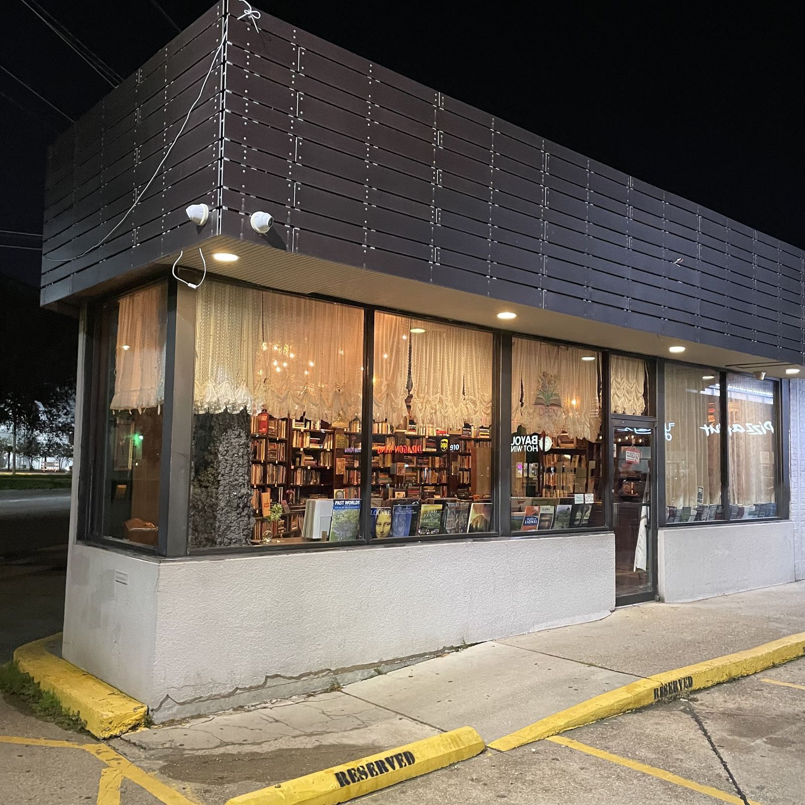 Two Foxes' Books storefront at night, windows glowing with lace curtains and shelves of books